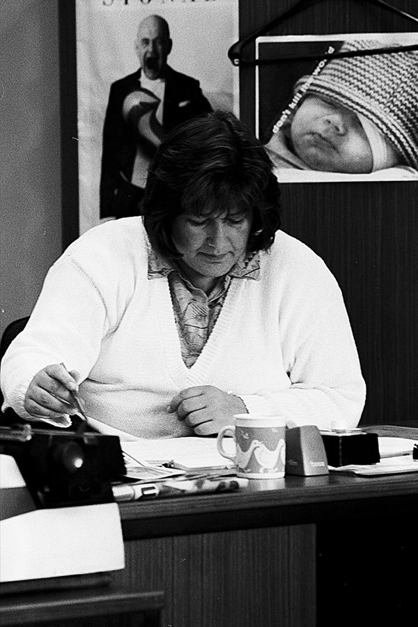 Eine Frau sitzt hinter einem Schreibtsich und wählt Fotos von einem Kontaktbogen aus