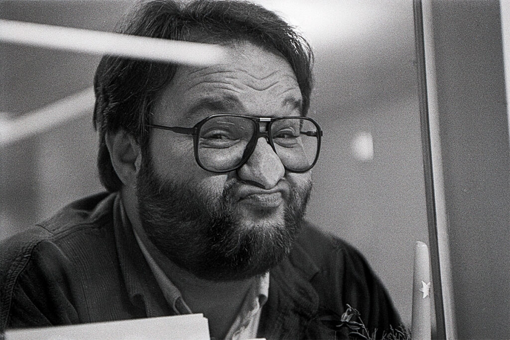 Ein freundlicher Mann mit Vollbart und Brille presst seien Nase von außen durch eine Glasscheibe.