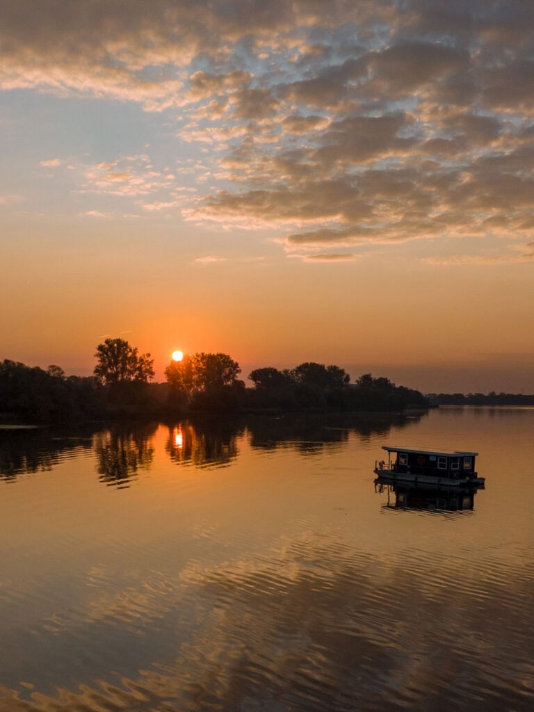 Ein Hausboot auf einem ruhigen Gewässer bei Sonnenuntergang im warmen Abendlicht. Foto: SaSch
