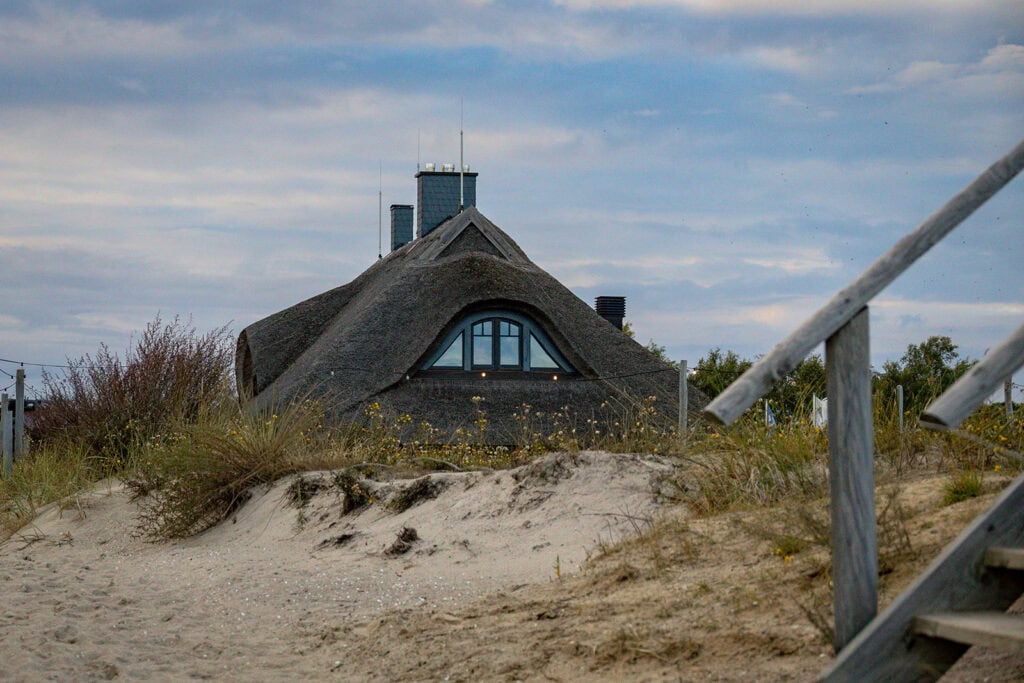 Strandhus Mönchgut: Reetdachhaus an der Ostsee mit Sanddünen und Treppe im Vordergrund.