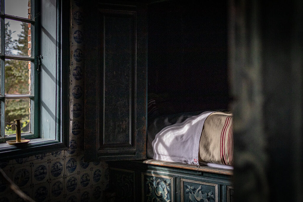 Historisches Schlafzimmer mit antiker Einrichtung und Tageslicht durch Fenster.
