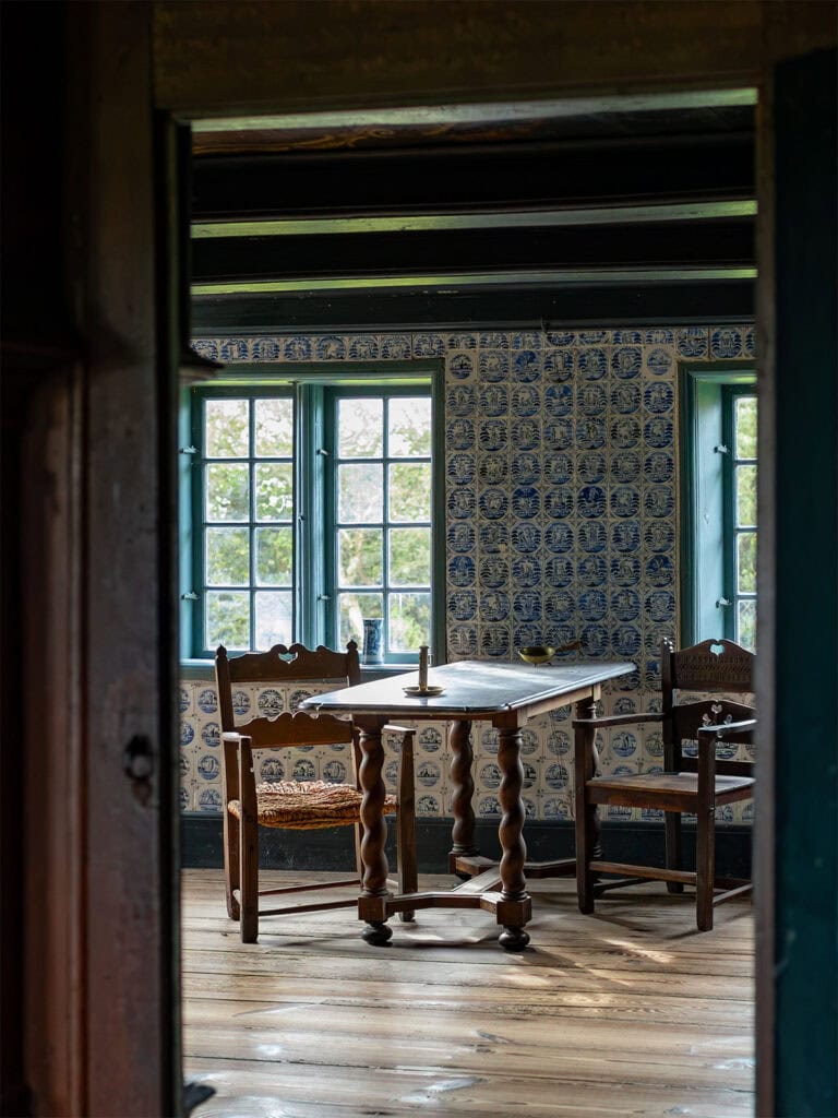 Altes Zimmer mit Holzstühlen, Tisch und blauer Fliesenwand.