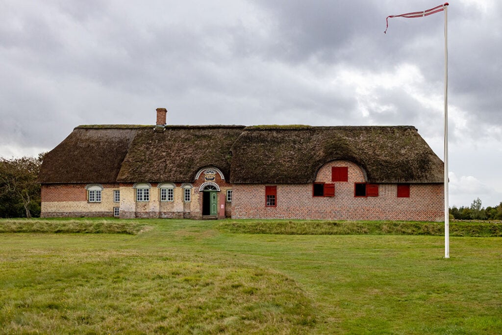 Historisches Haus mit Reetdach und rot-weißen Fenstern unter dunklem Himmel.